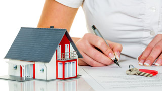 Eine Frau unterschreibt ein Dokument, daneben steht ein Miniaturhaus und liegt ein Schlssel