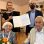 Ein älteres Paar sitzt vor Bezirksvorsteherin Christine Dubravac-Widholm und einem Mann mit Urkunde