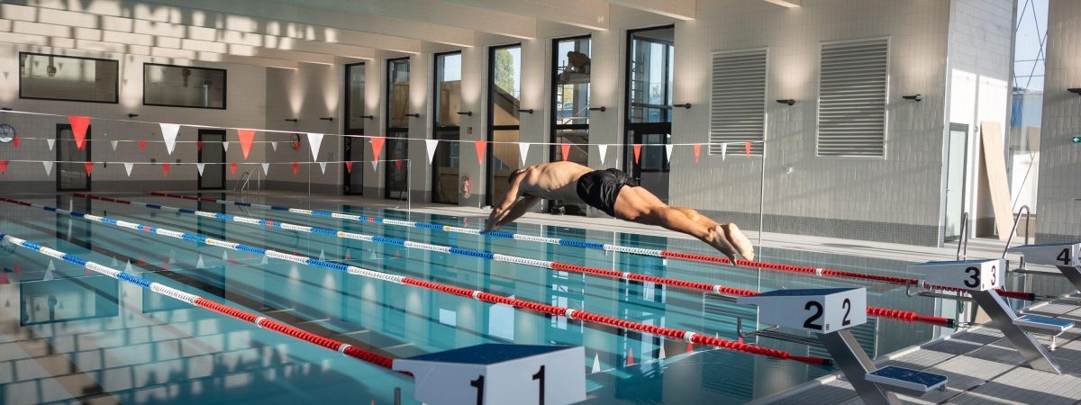 copyright: Stadt Wien / David Bohmann Ein Schwimmer springt in ein Schwimmbecken mit Schwimmbahnen.