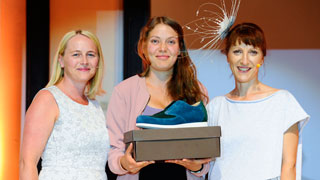 Drei Frauen nebeneinander, ein von ihnen hlt eine Schuhschachtel auf der ein blauer Schuh platziert ist
