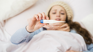 A young woman lying in bed looking at a clinical thermometer