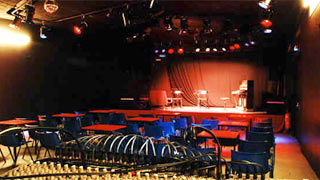 Konzertsaal: Mischpult, Stuhlreihen, im Hintergrund hell beleuchtete Bhne mit Sthlen