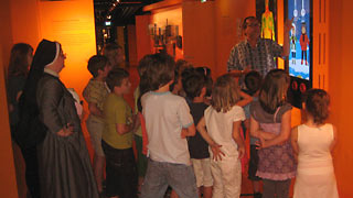 Man explaining part of the exhibition to a group of children.