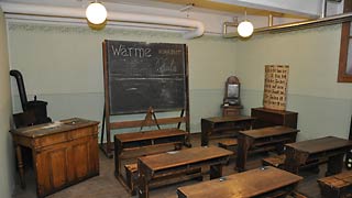 Antiquated schoolroom with desks and black board.