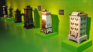 Several stoves in a row, displayed in a green exhibition room.