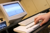 Hand tastet ber Braillezeile, im Hintergrund Bildschirm und Tastatur