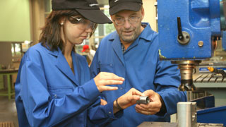 Mann hilft junger Frau bei einer technischen Ttigkeit an einer Maschine