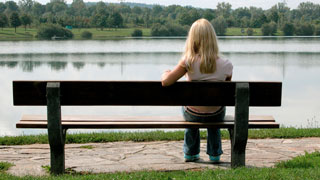 Blonde Frau sitzt auf einer Parkbank vor einem Gewsser