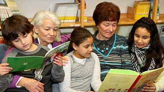 İki gönüllü, üç çocukla birlikte kitap okuyorlar.