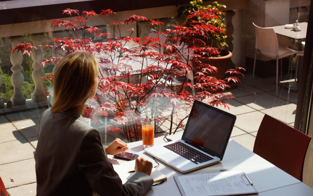 Frau sitzt mit ihrem Laptop auf einer Terrasse mit Pflanzen
