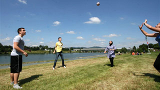 Four people playing volleyball on a meadow next to the water.