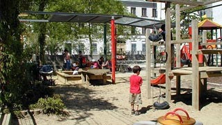 Kinder spielen auf Sandspielplatz mit Federwippe und Kletterturm