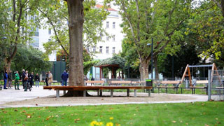 Zentraler Bereich in einem Park mit Sitzgelegenheiten und Spielplatz, im Vordergrund eine Wiese und Blumen