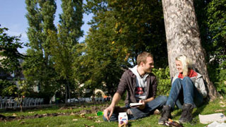 2 Menschen sitzen auf der Wiese unter einem Baum