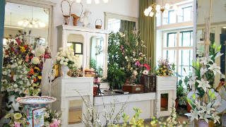 Ein wei gehaltener Raum voller Blumen, im Hintergrund Spiegel, weie Ksten und Kommoden