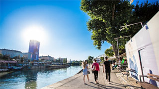 A group of young people strolling along the Donaukanal in the sun.