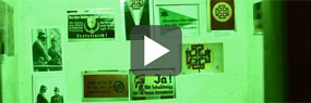 Videoausschnitt mit Play-Button: Propagandabilder aus dem Zweiten Weltkrieg in einem grün ausgeleuchteten ehemaligen Luftschutzbunker