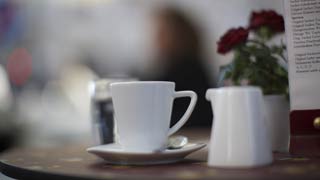 Stol u kafeu sa šalicom kave, posudom s mlijekom i cvijetom kao dekoracijom.
