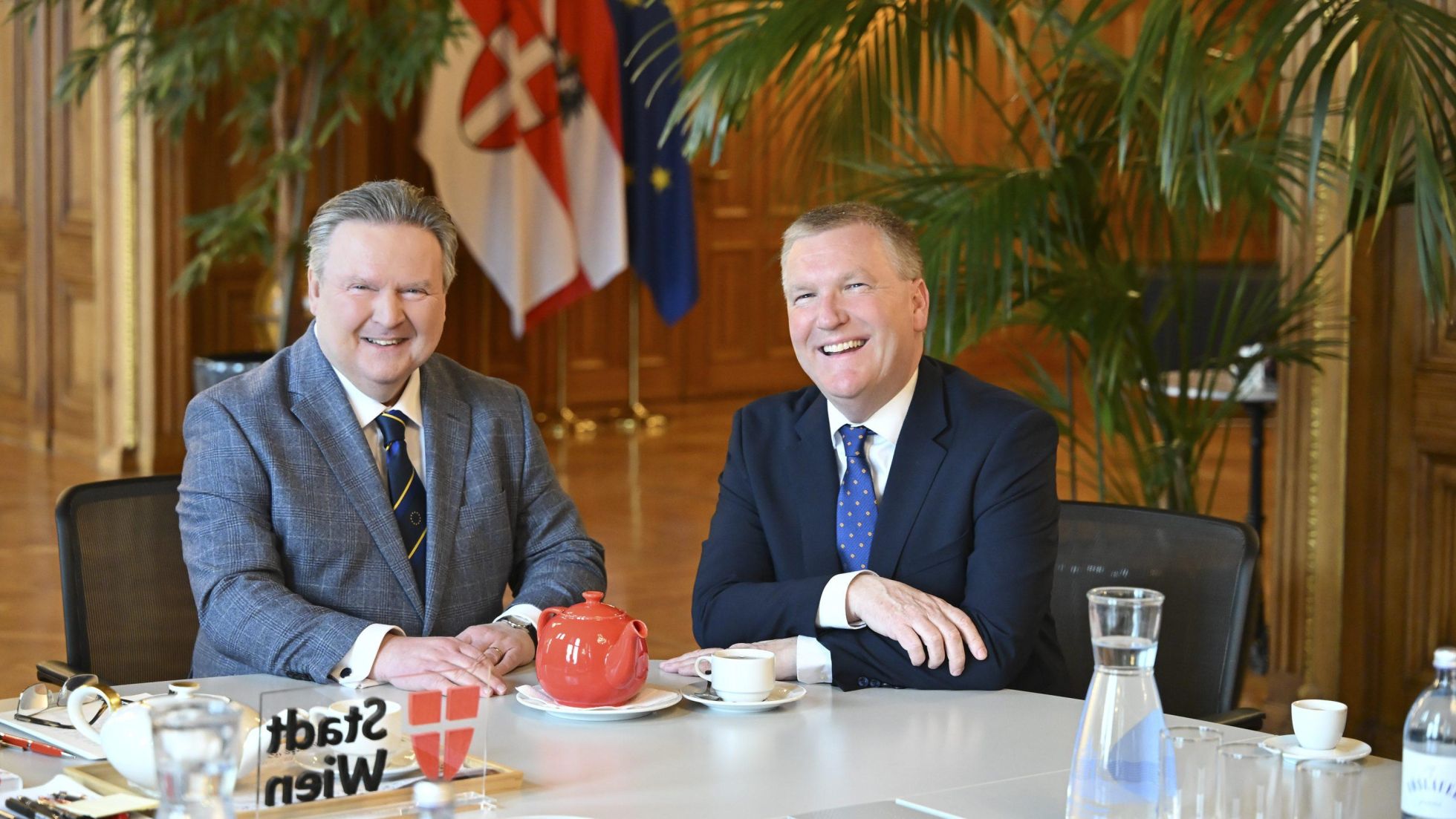 copyright: Stadt Wien / Christian Jobst Ludwig und McGrath sitzen an einem Tisch und lächeln gemeinsam in die Kamera.