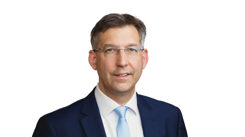 Ein Mann mit Brille und Anzug lächelt in die Kamera