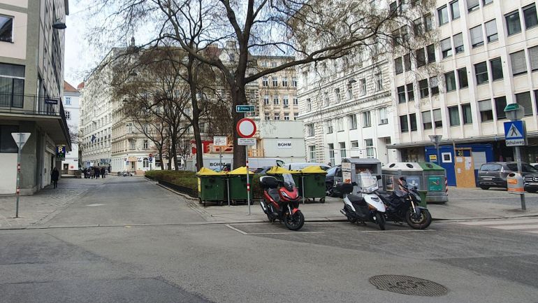 copyright: BV 1 Platz mit Bäumen in der Mitte, rundherum Altbauten, Gehweg, Straße und parkende Mopeds.
