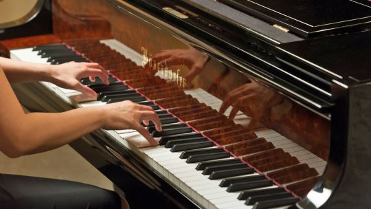 Eine Frau spielt Klavier; man sieht nur den Ausschnitt ihrer Hände auf den Tasten