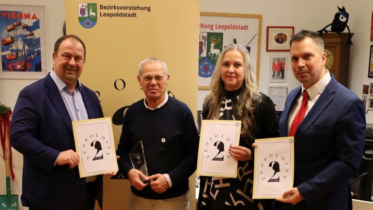 Gruppenfoto: 3 Männer und 1 Frau halten Urkunden vor einem Roll-Up in einem Raum mit Parkettboden.