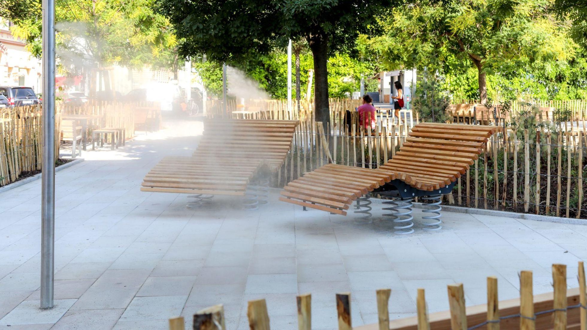 copyright: Stadt Wien/Christian Fürthner Nebelstelen vor modernen Liegestühlen aus Holz auf heller Pflasterung, im Hintergrund Bäume.