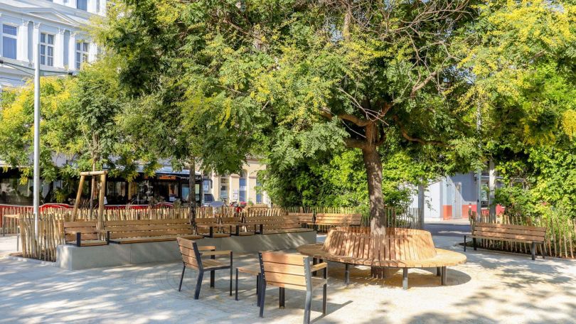 copyright: Stadt Wien/Christian Fürthner Sitzgelegenheiten rund um einen großen blühenden Baum, helle Pflasterung und im Hintergrund die weitläufige Parkanlage