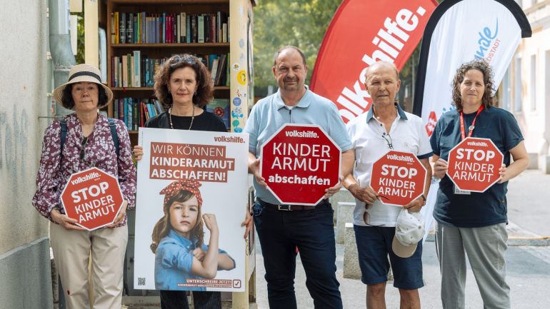 5 Personen halten Schilder mit der Aufschrift "Stop Kinderarmut" hoch.