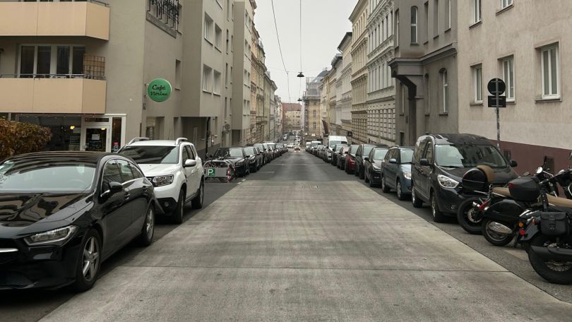 Blick in eine Straße mit parkenden Fahrzeugen entlang der Wohnhäuser links und rechts
