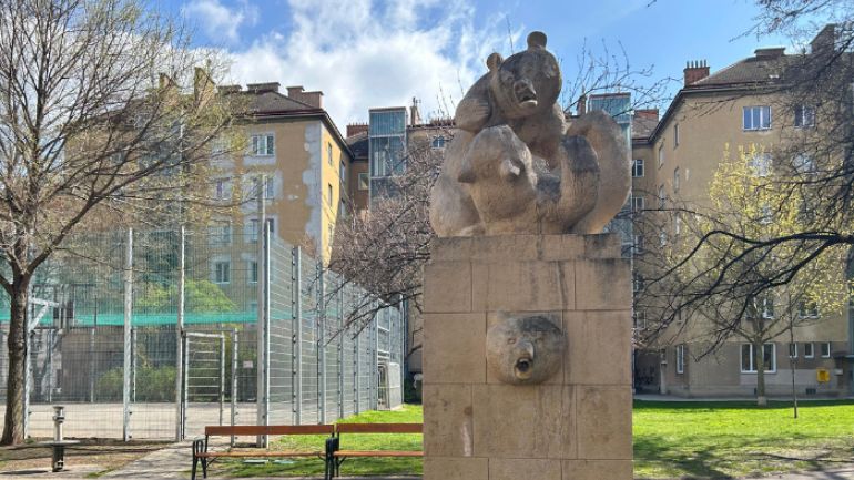 copyright: Thiemo Rydhlo Brunnen mit Statue von spielenden Bären vor einem Ballspielkäfig und Bänken