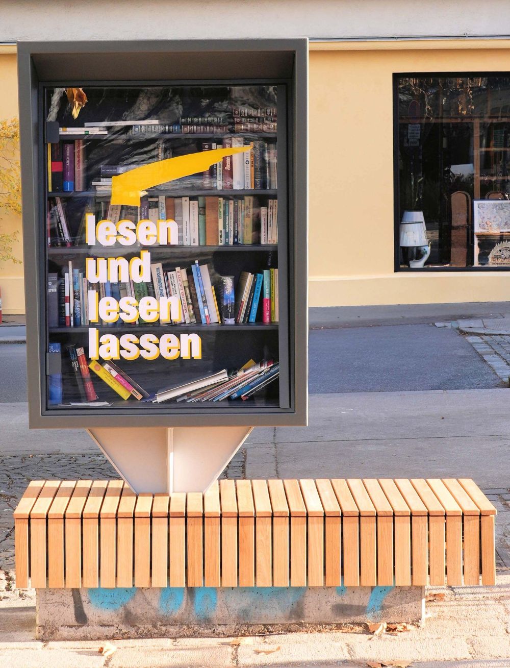 Bücherschrank mit Aufschrift "lesen und lesen lassen" mit Sitzbank aus Holz.