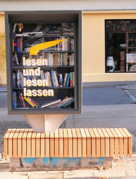 Bücherschrank mit Aufschrift "lesen und lesen lassen" mit Sitzbank aus Holz.