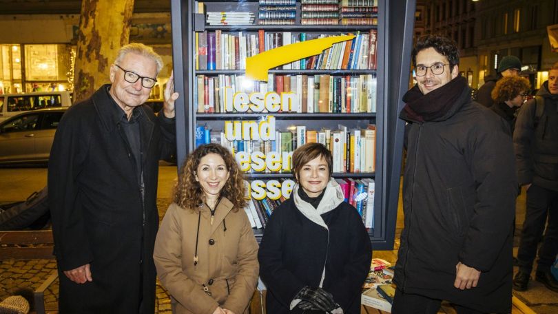 4 Personen im Mantel beim Bücherschrank.
