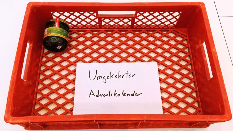 copyright: Daniel Böhm Roter Plastikbehälter mit Text "Umgekehrter Adventkalender" mit Honigglas als erste Gabe.
