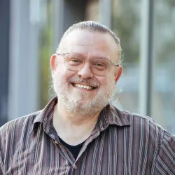Portrait von einem Mann mit grauen Haaren und grauen Bart und einer Brille