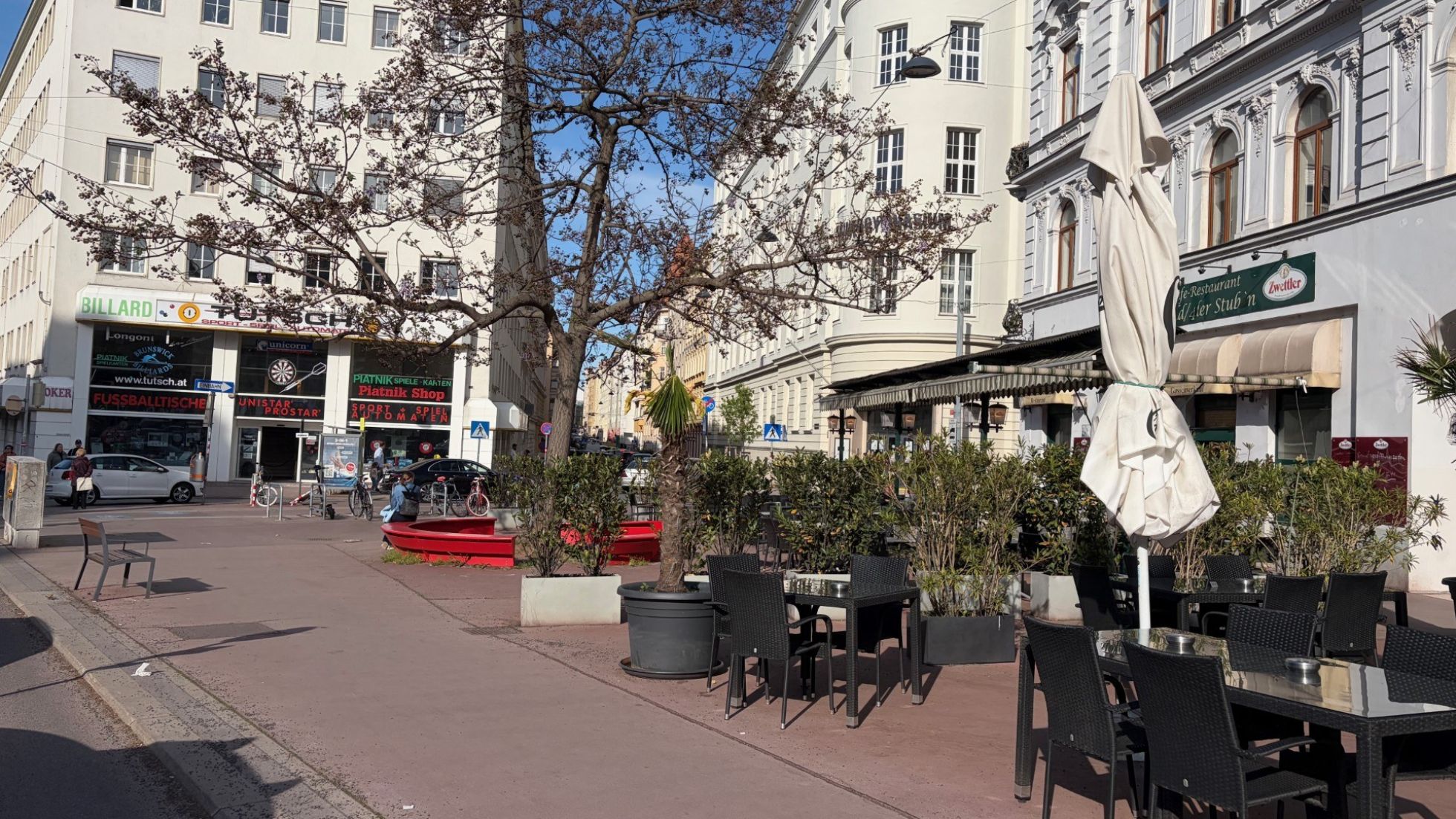 copyright: Gebietsbetreuung*Stadterneuerung/Christina Schneider Ein asphaltierter Platz zwischen Altbauten mit Pflanzen, Tischen und Stühlen