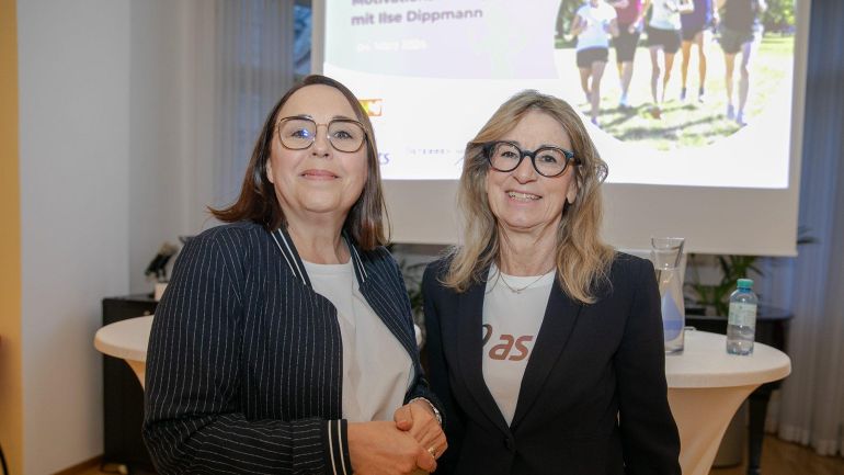 2 Frauen stehen vor einer Leinwand auf der ein Foto mit Läuferinnen zu sehen ist.