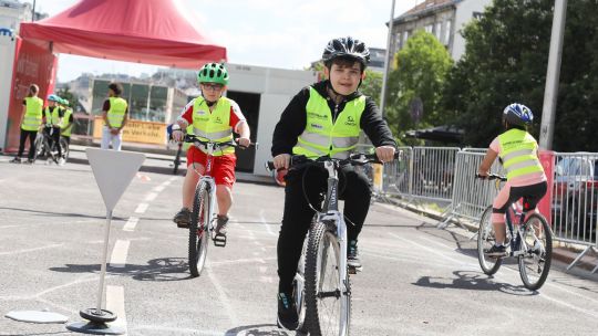 Kinder in gelben Warnwesten und Helm fahren mit dem Rad an einer vorgegebenen Strecke am Übungsplatz