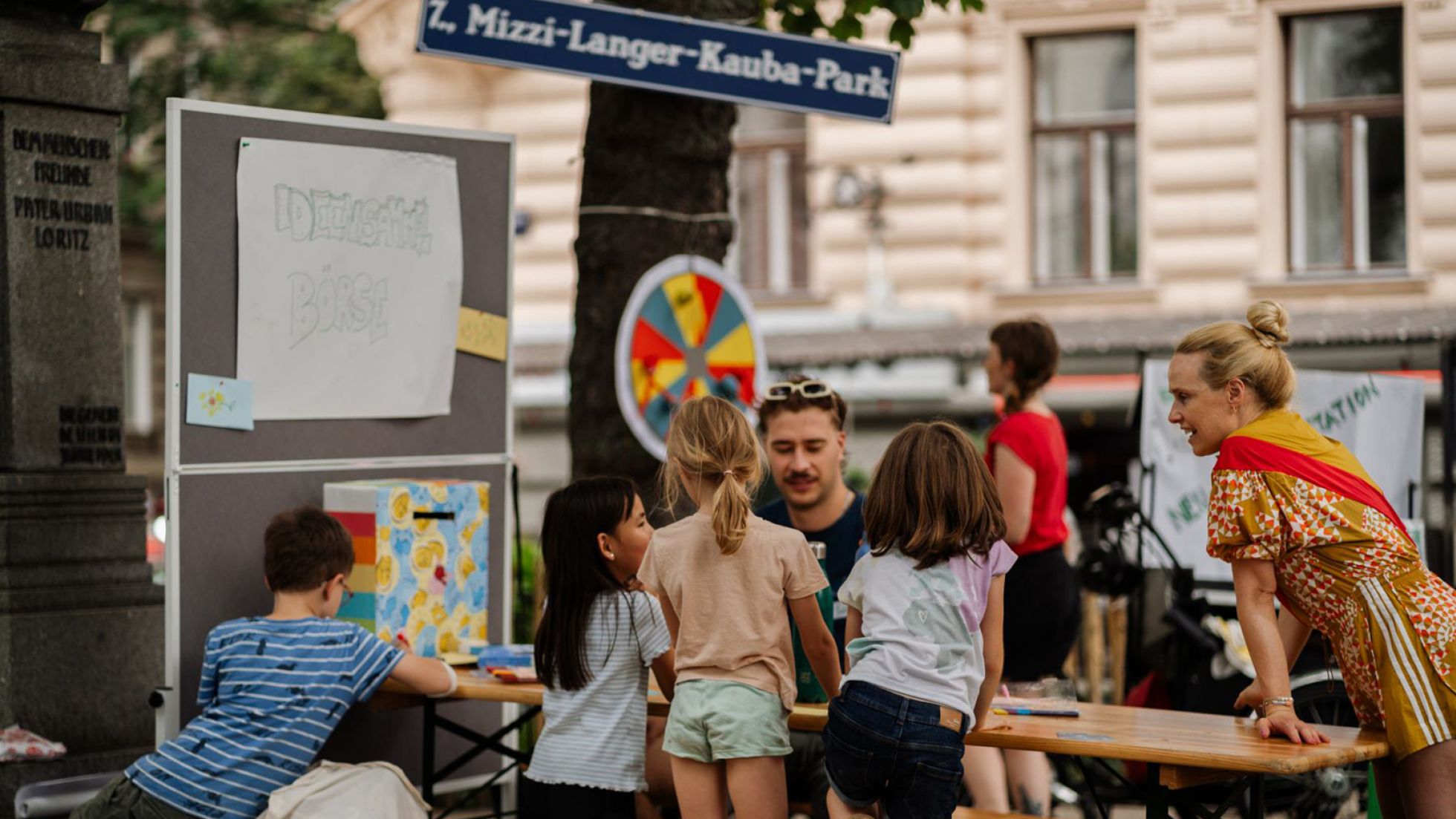 Mehrere Kinder und 2 Erwachsene unterhalten sich an einem Tisch