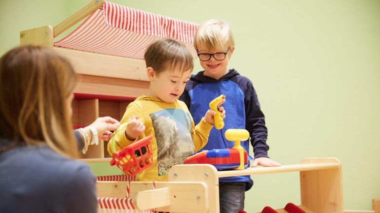 2 kleine Kinder spielen in einem Kaufmannsladen aus Holz.