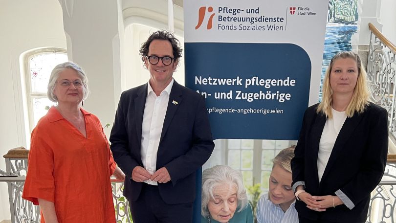 copyright: BV 7 Ein Mann steht zwischen 2 Frauen. Hinter ihnen ist ein Plakat mit der Aufschrift "Netzwerk pflegende Angehörige" sowie einer älteren und einer jüngeren Frau zu sehen.