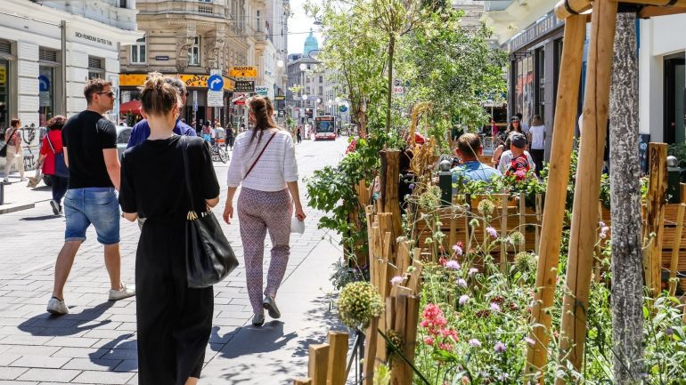 Besucherinnen und Besucher spazieren durch die begrünte Neubaugasse