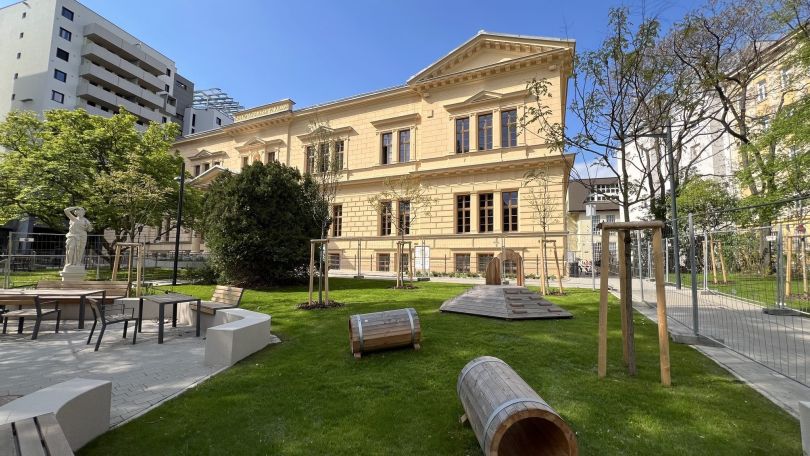 Renovierter Altbau, davor Bäume, Sitzmöglichkeiten und Grünflächen