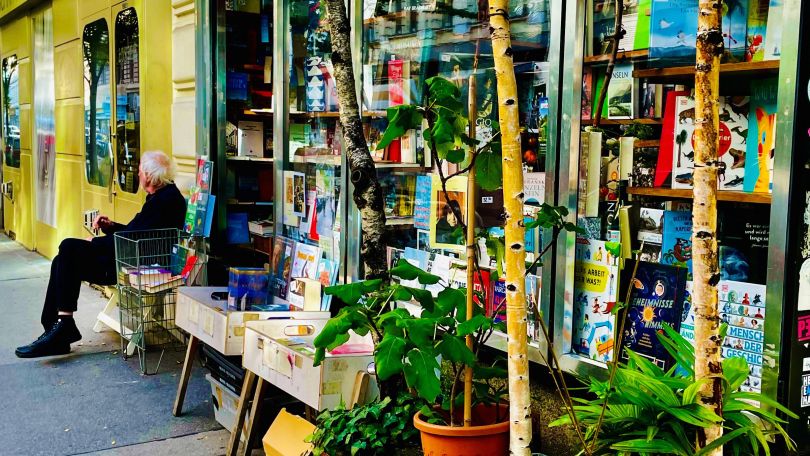 copyright: Cornelia Ehmayer Ein Mann sitzt vor einem Bücherladen, vor dem viele grüne Pflanzen stehen