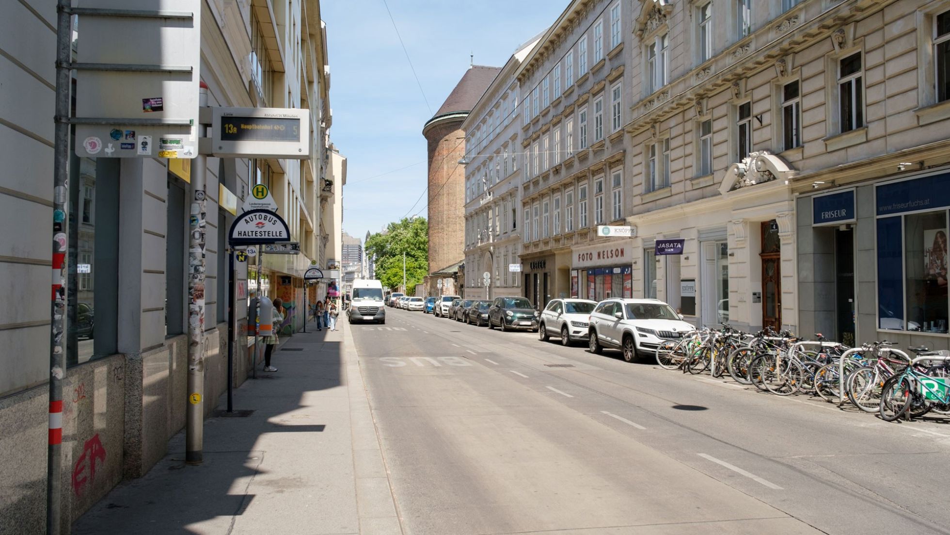 Straße mit Altbauten, Bushaltestelle, geparkten Autos und Fahrrädern