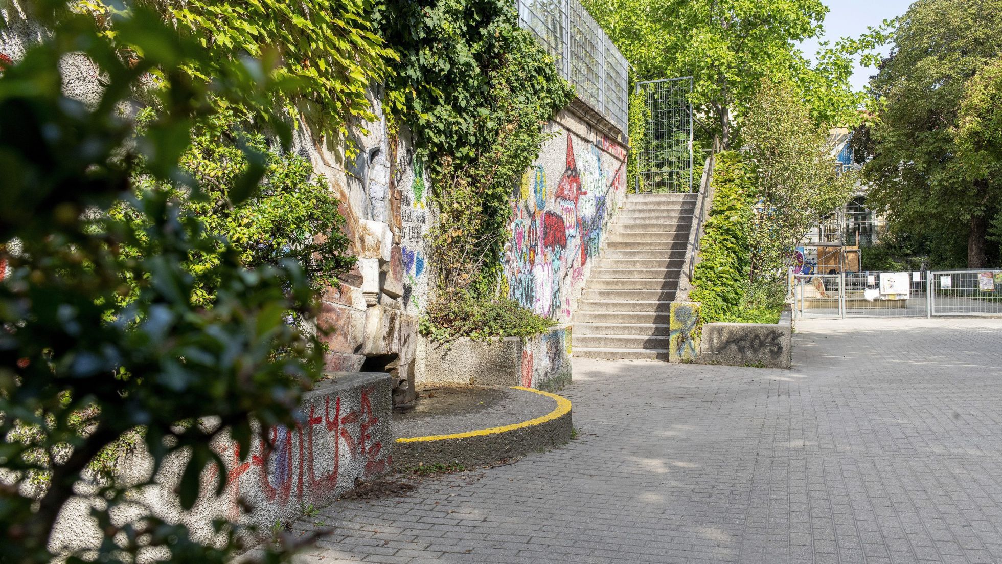 copyright: Kollektiv Fischka / Kramar Eine Betontreppe führt zu einem Betongebäude. Die Außenmauer ist mit Graffiti besprüht und mit Pflanzen bewachsen.
