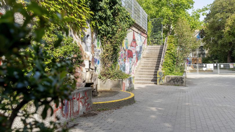 copyright: Kollektiv Fischka / Kramar Eine Betontreppe führt zu einem Betongebäude. Die Außenmauer ist mit Graffiti besprüht und mit Pflanzen bewachsen.