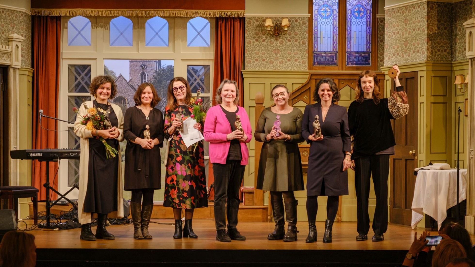 Gruppenfoto von 7 Frauen auf der Bühne mit Auszeichnungen und Blumensträußen.